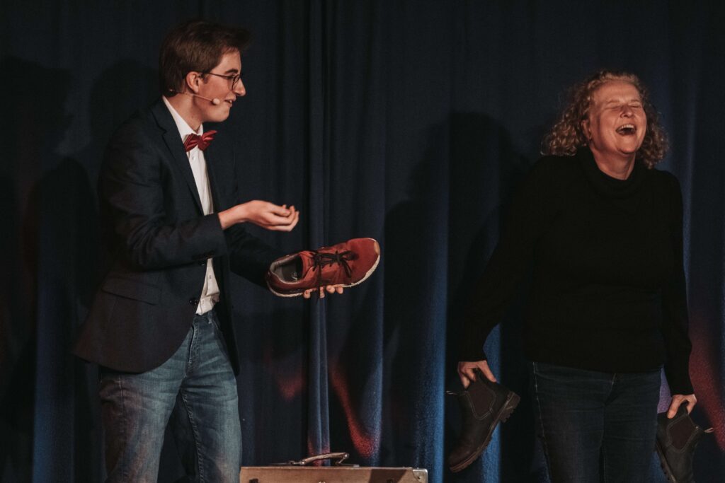 Zauberer Tjark Schlößer steht bei einem Zaubertrick mit einer Zuschauerin auf einer Bühne in Hamburg.